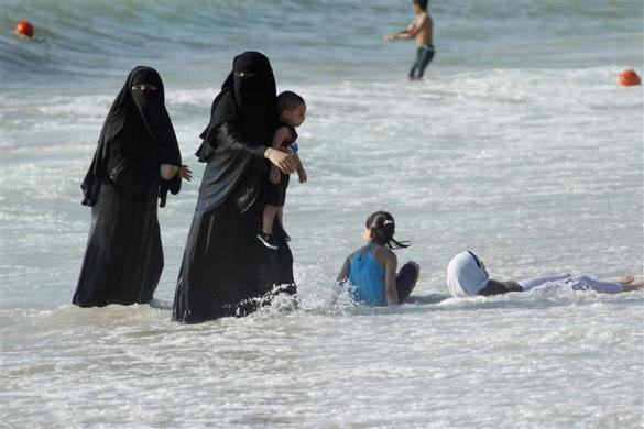 Veiled women, with their children, enjoy the warm weather on a beach at the port city of Sidon in southern Lebanon